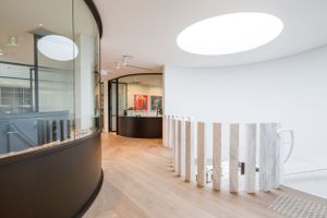 Modern office hallway with curved glass walls, wooden slats, and dramatic circular skylight.