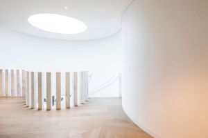Minimalist white gallery space with circular skylight and wooden columns.
