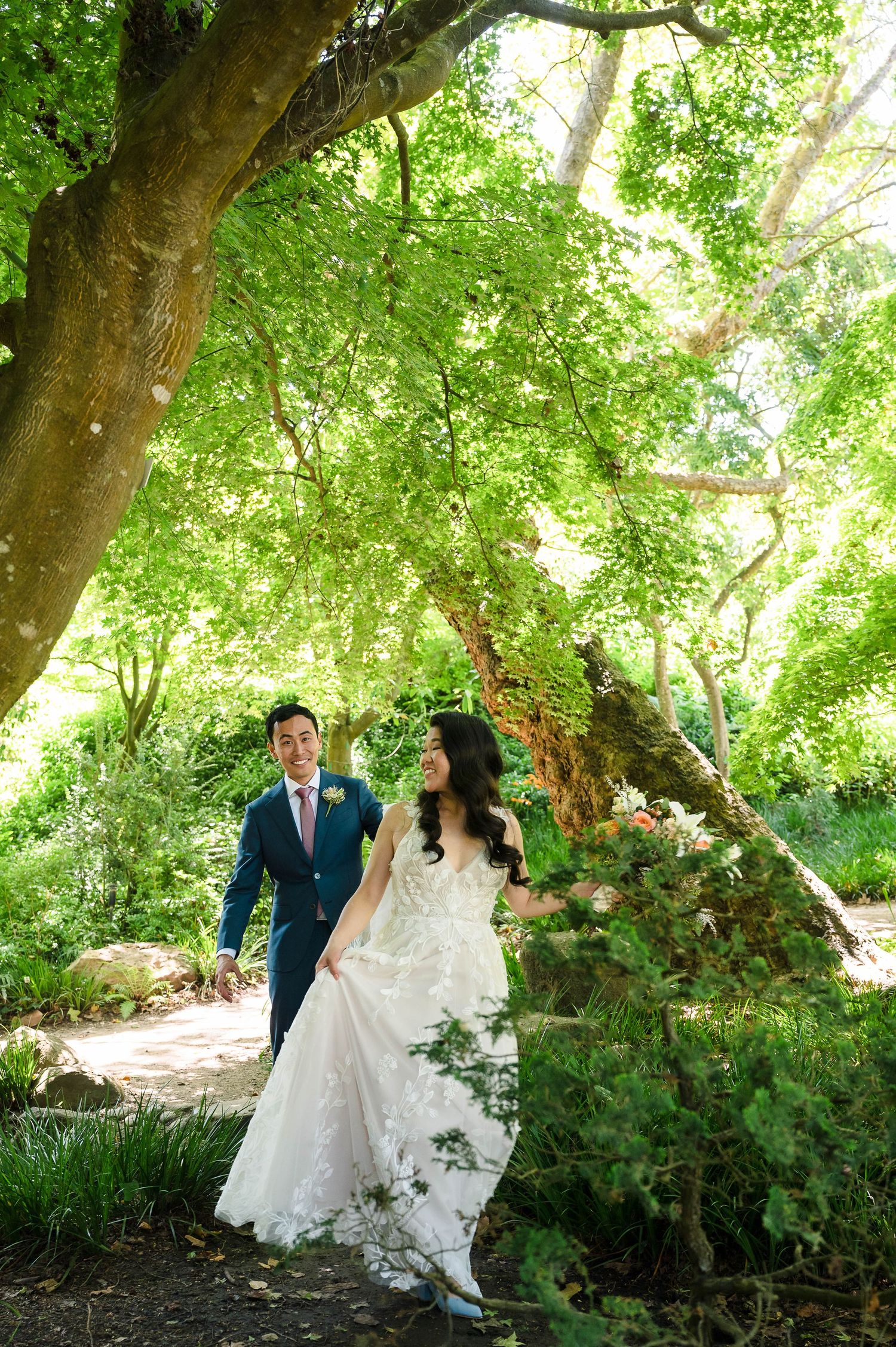 A romantic woodland scene with a couple walking beneath a canopy of lush green maple trees.