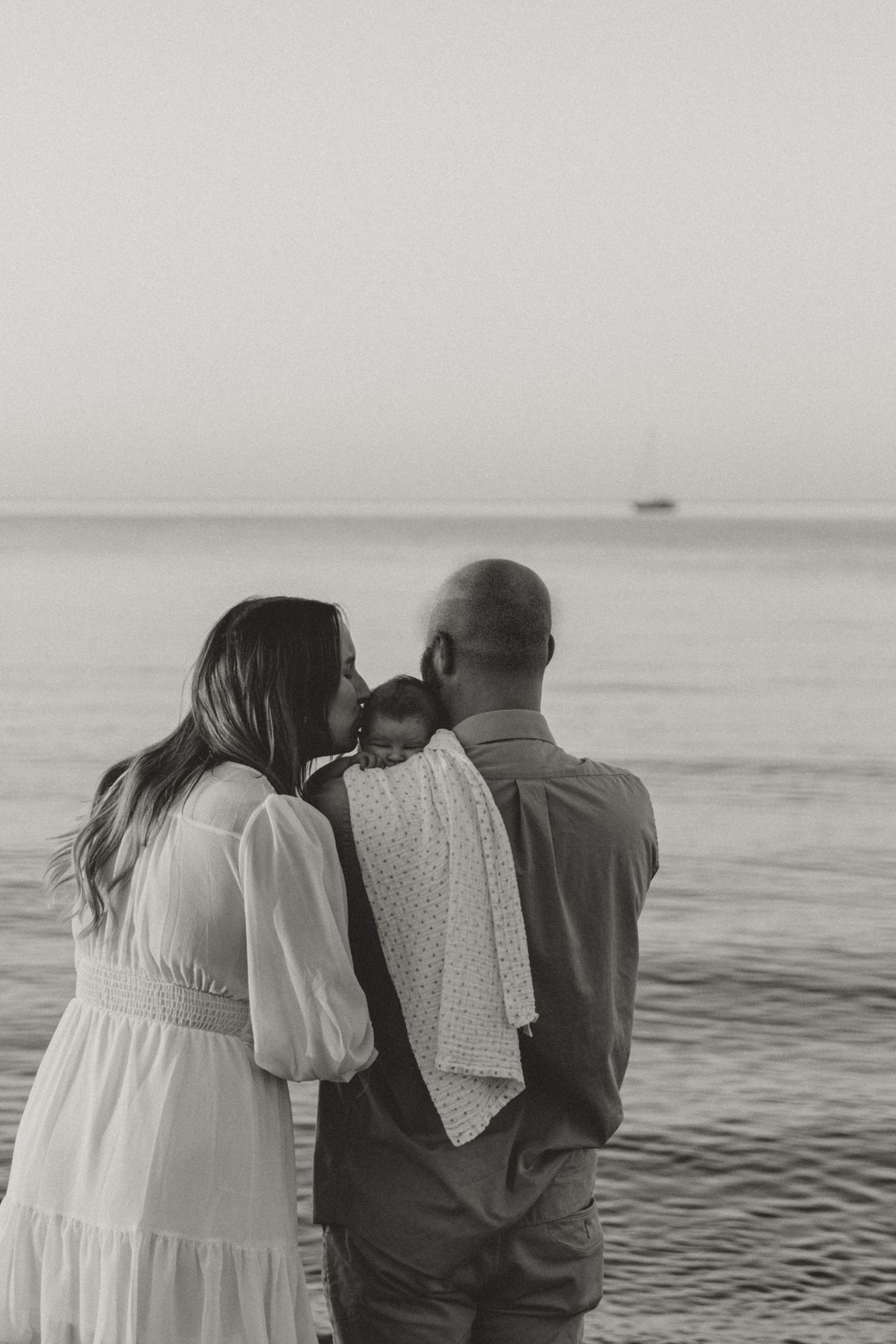 Couple in white attire gazes at ocean during sunset on beach.