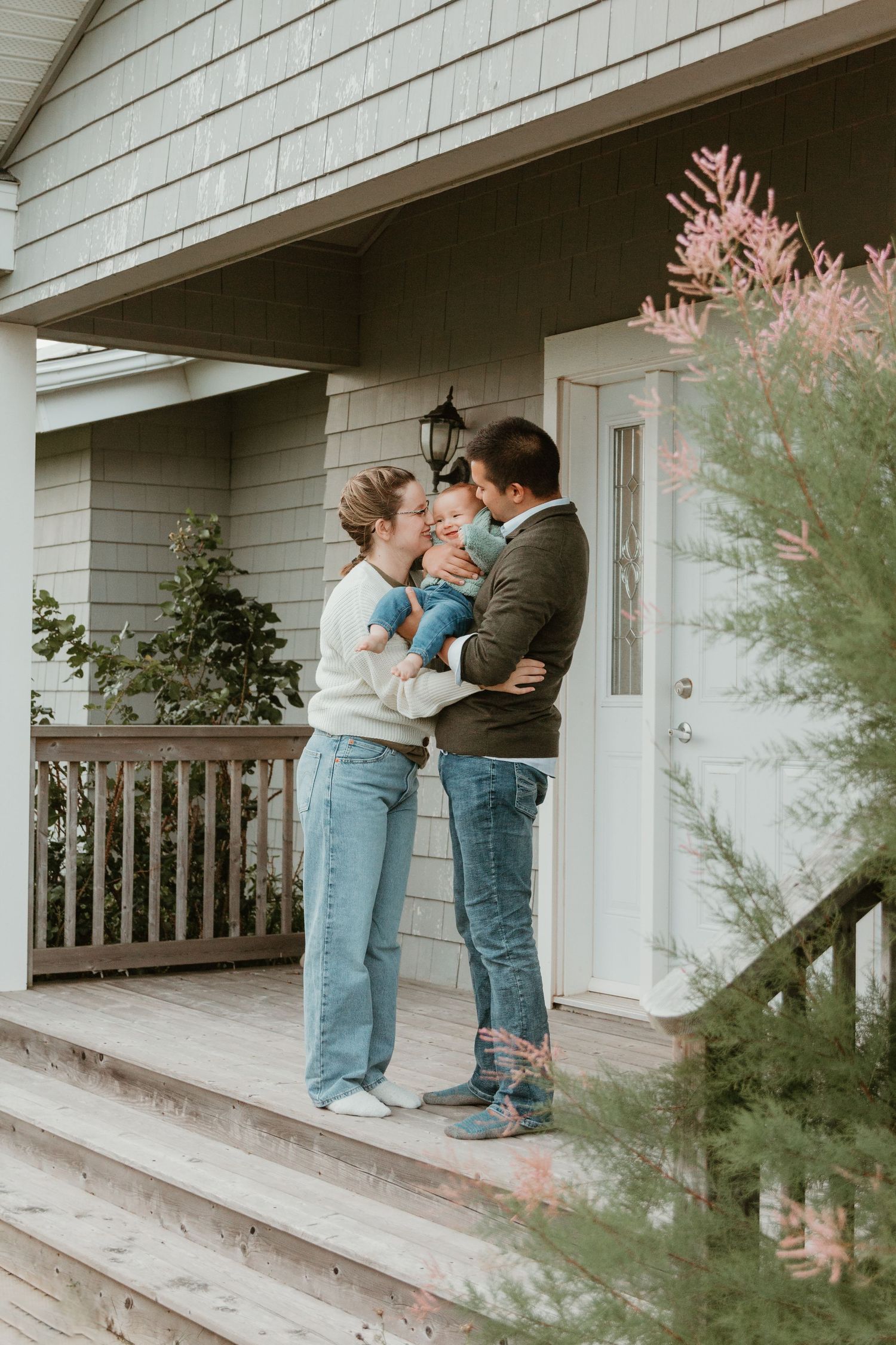Sweet family moment on front porch of white house with decorative plants.