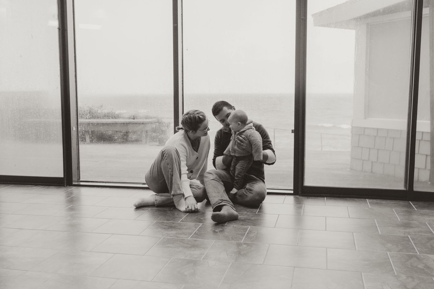 Black and white photo of family sitting together on floor near window.