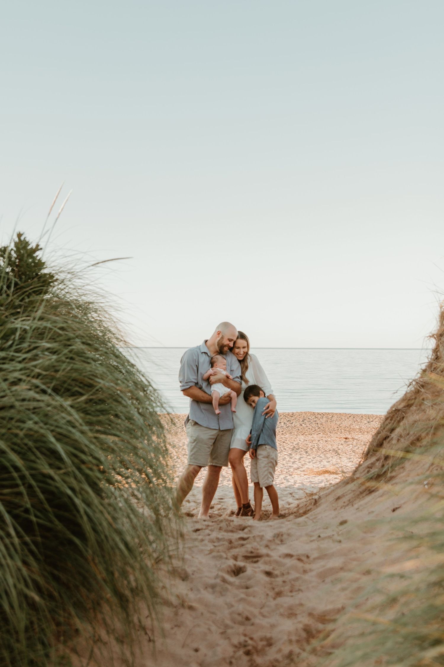 Family standing together between beach grass dunes with ocean view.
