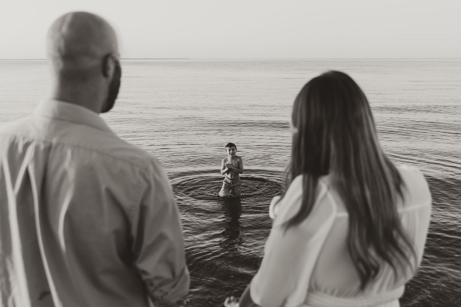 Couple watches figure playing in ocean waves from shoreline.