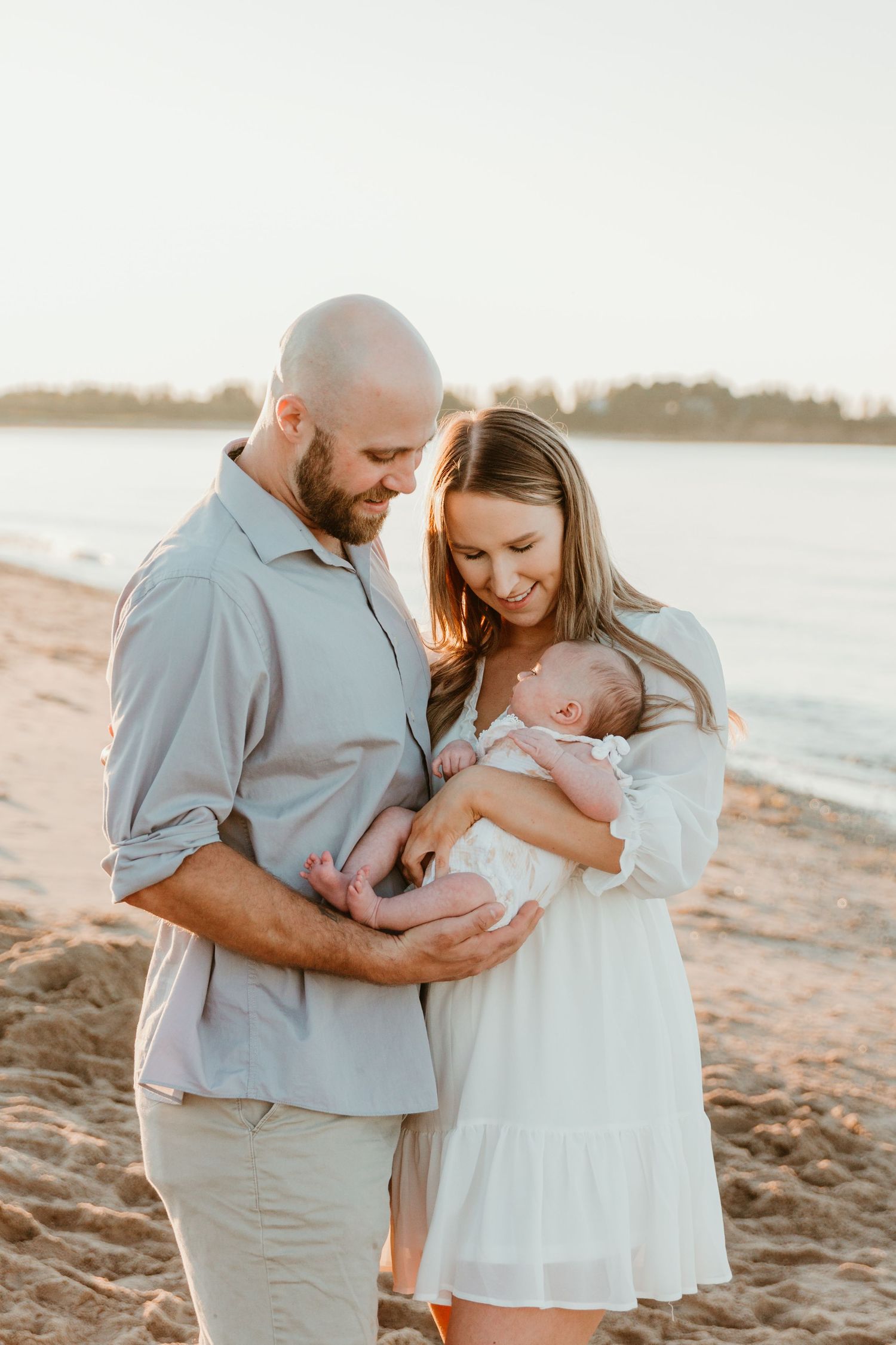 Family sharing intimate moment with newborn baby on beach at sunset.