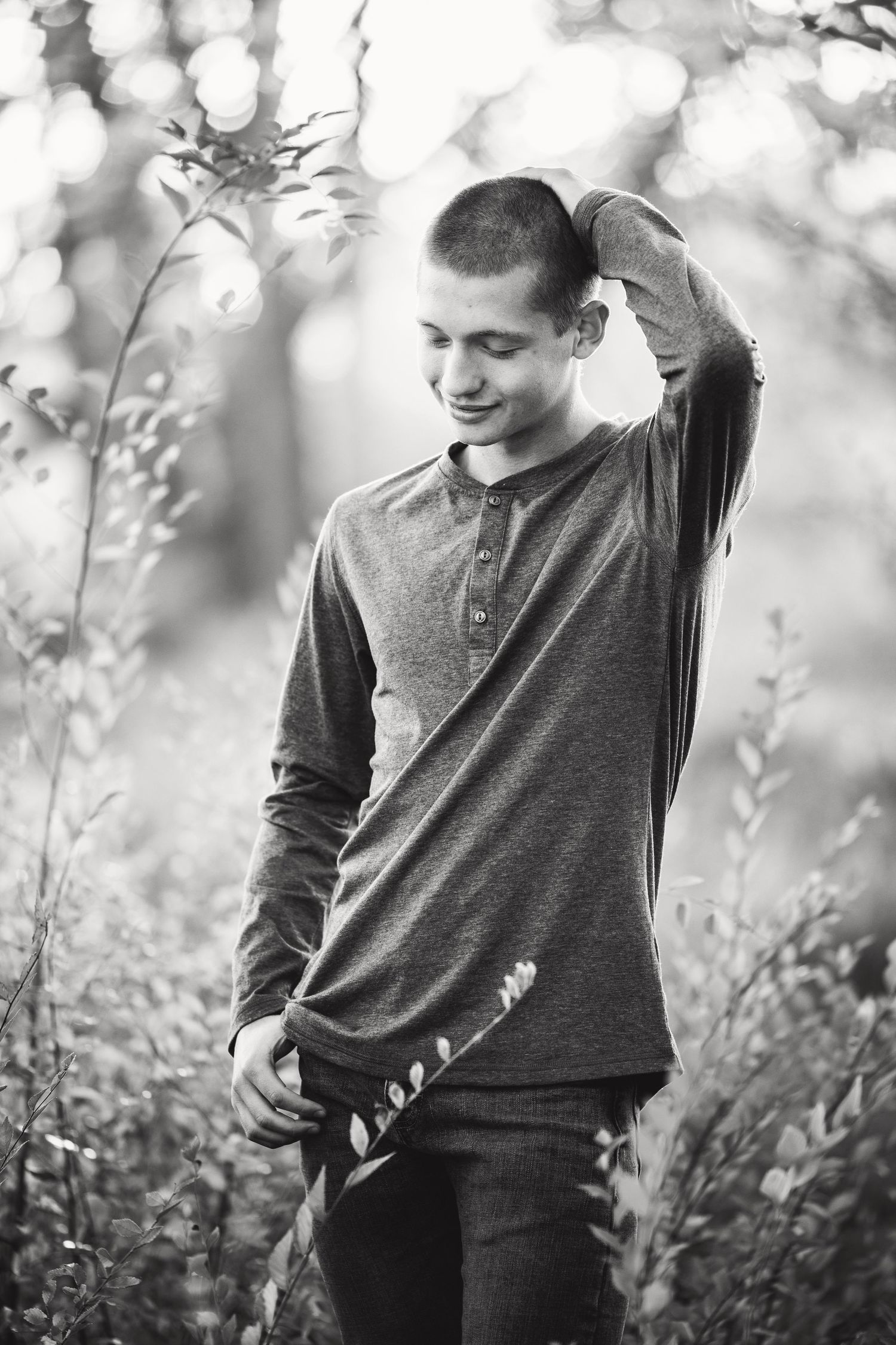 black and white image of a senior boy rubbing the back of his head and looking down in a beautiful forest