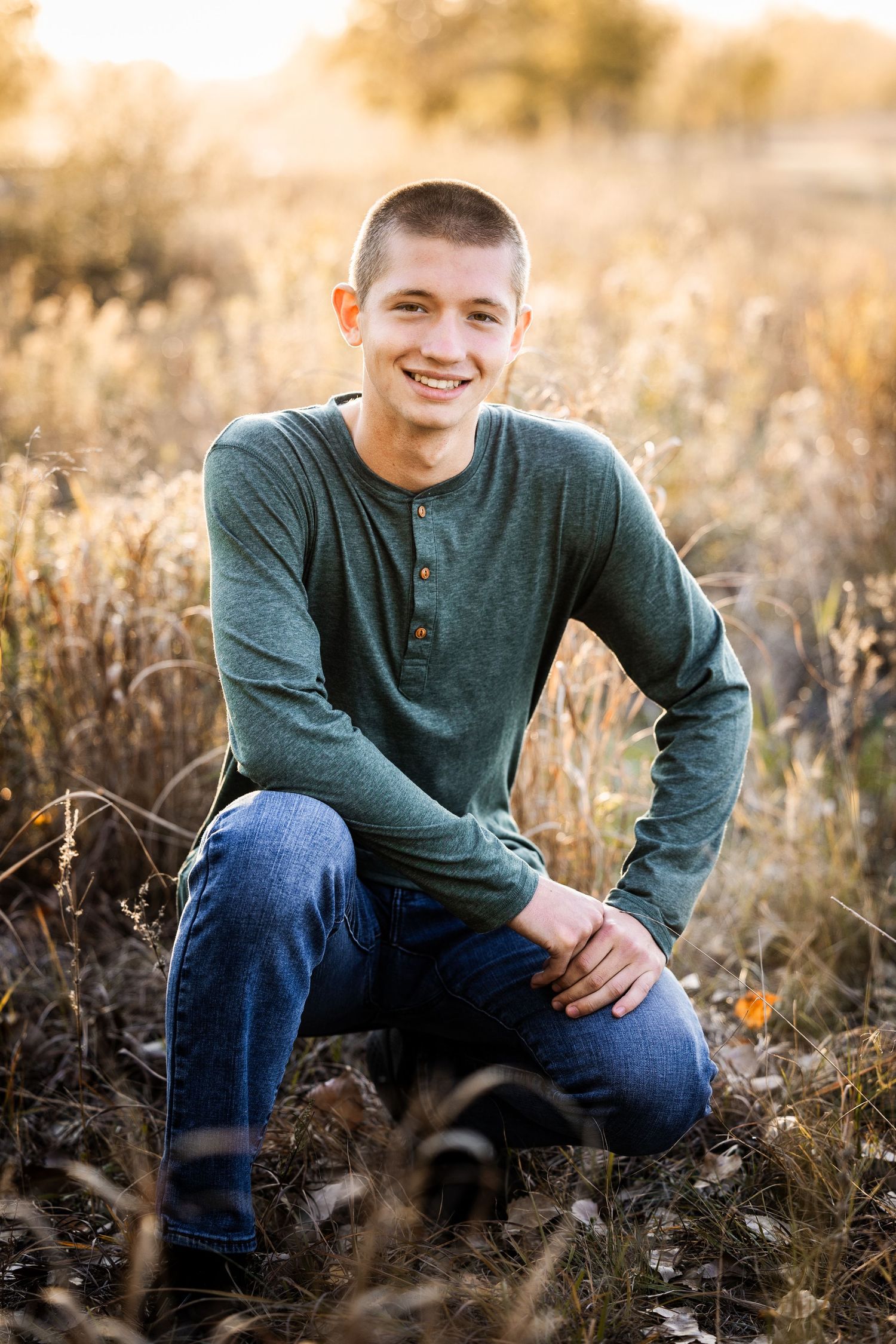 teenage boy in a green shirt kneeling down in a golden field