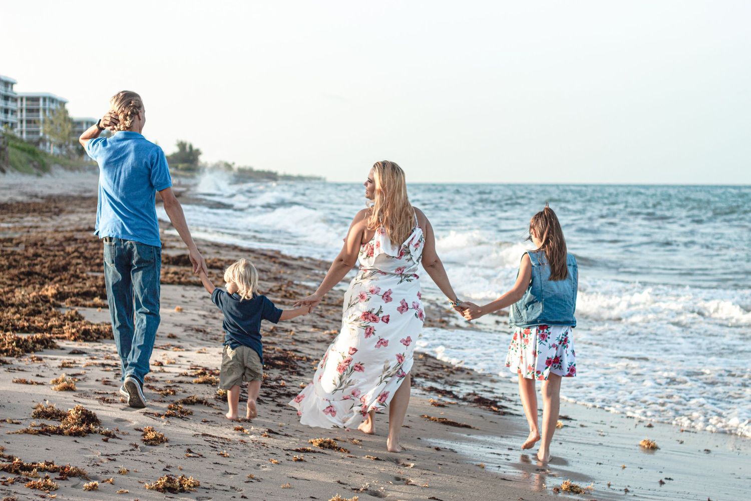 Group walking and holding hands together on a scenic beach with waves crashing along the shoreline at sunset on Lake Worth Beach.