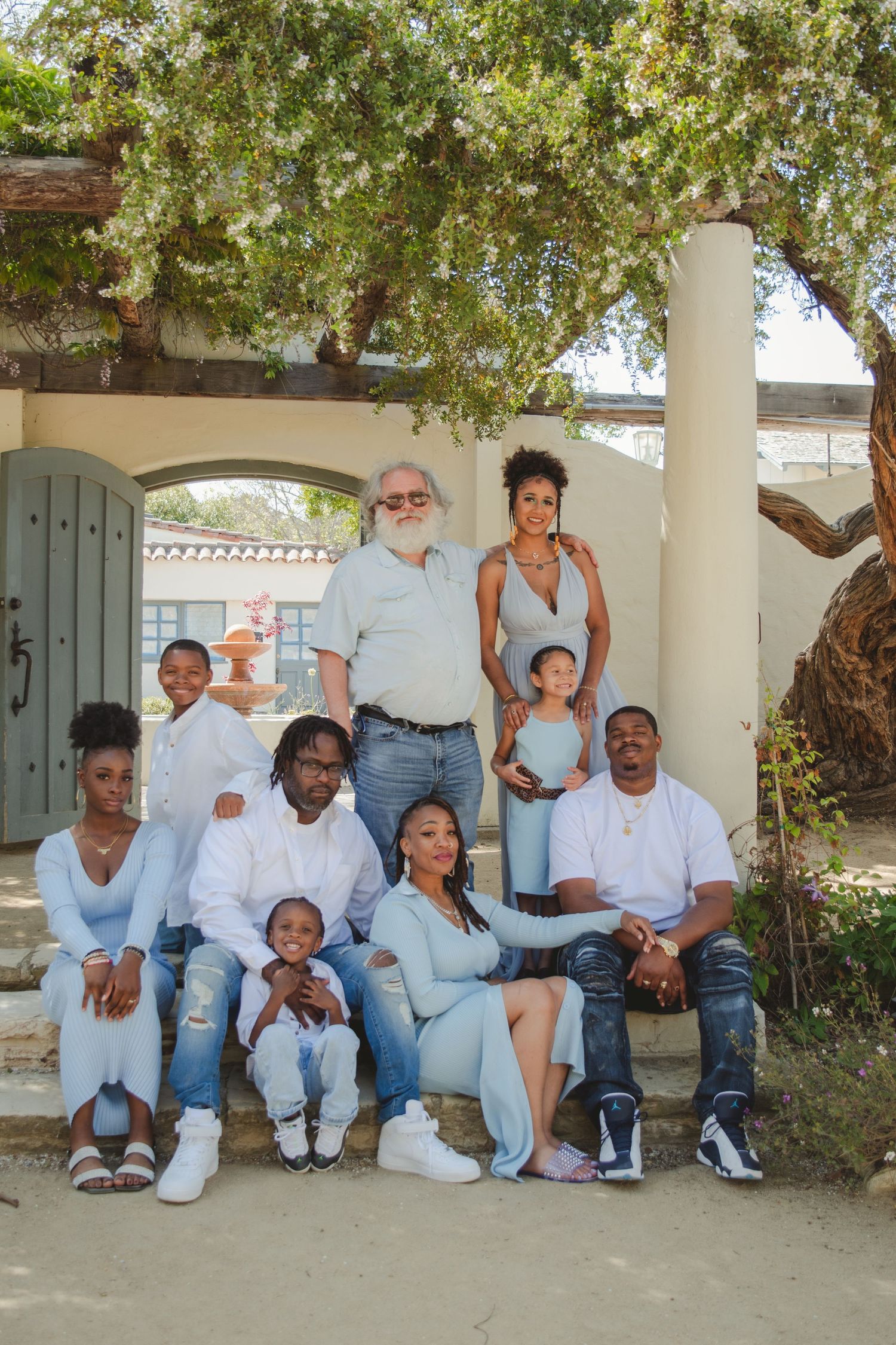 Multi-generational family group portrait on outdoor steps under a flowering tree.