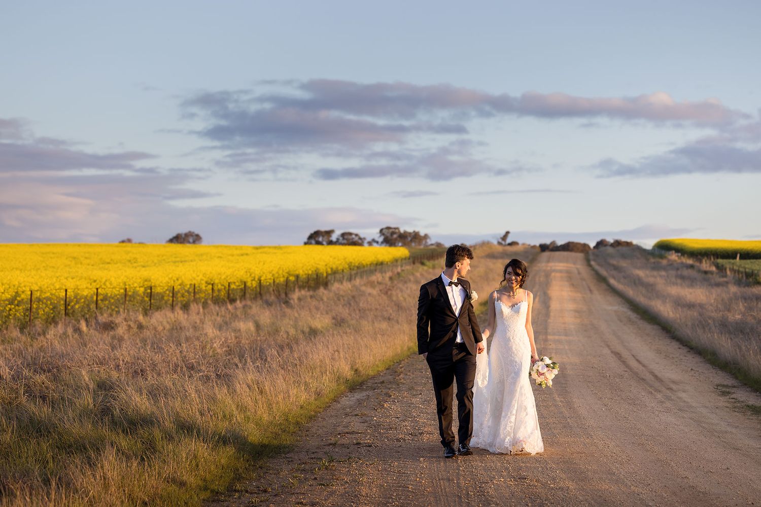 Bride and Groom standing on a dirt road beside a Canola Field at sunset on their De Bortoli Rutherglen Estate wedding