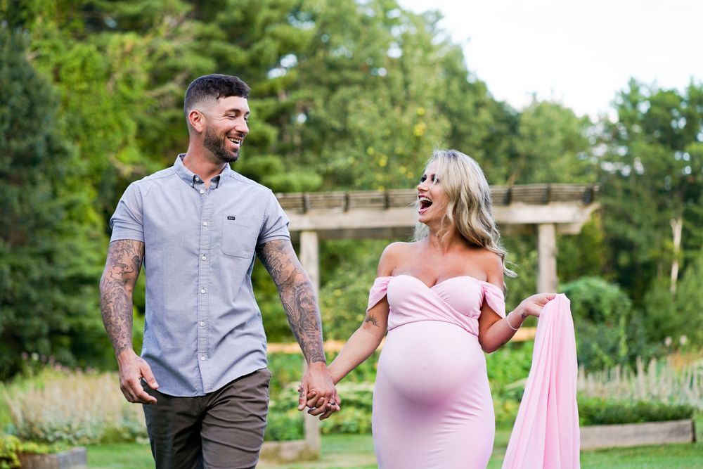 Couple walking hand in hand through garden, expecting mother wearing pink dress.