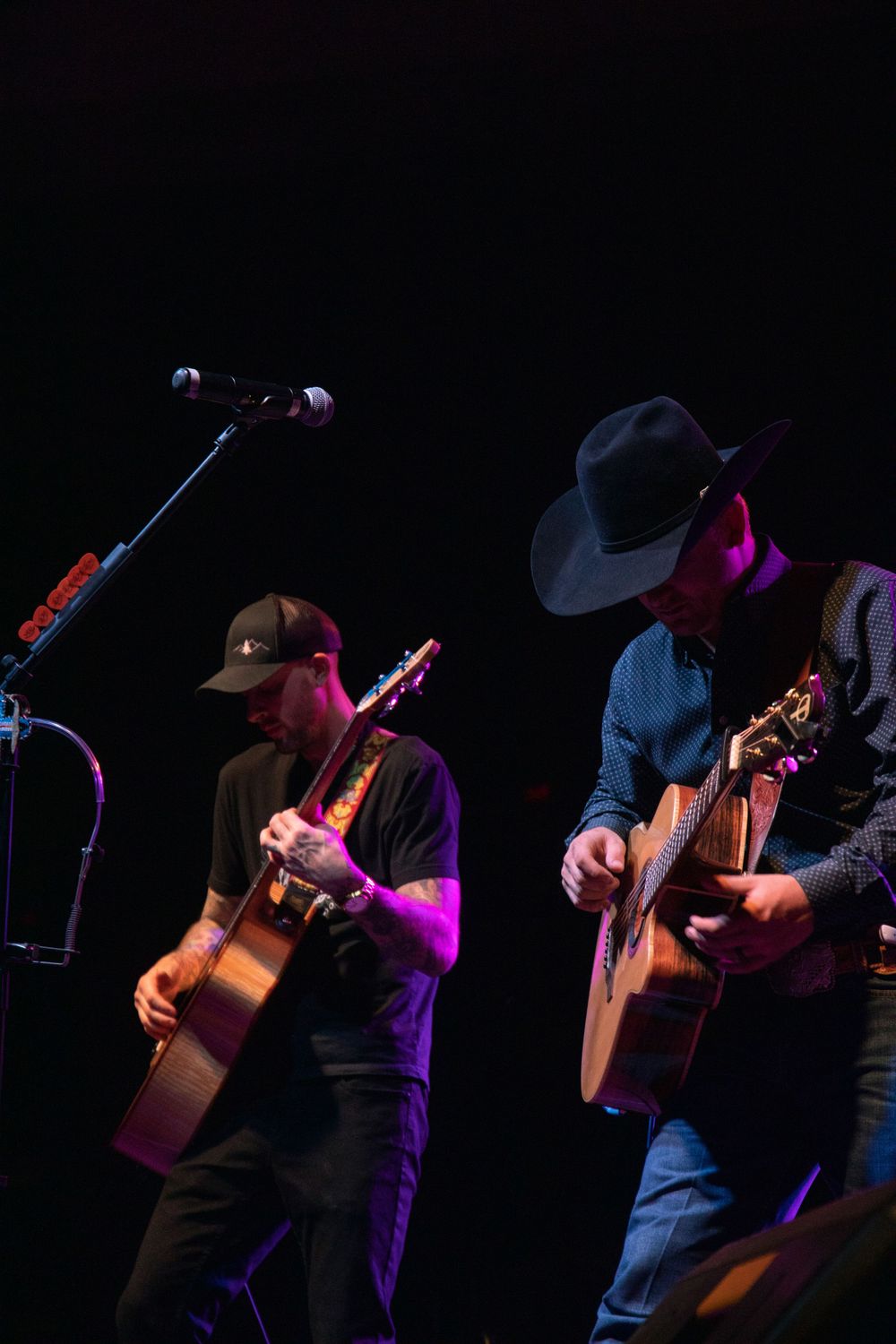 Musicians in cowboy hats perform with acoustic guitars on a dimly lit concert stage.