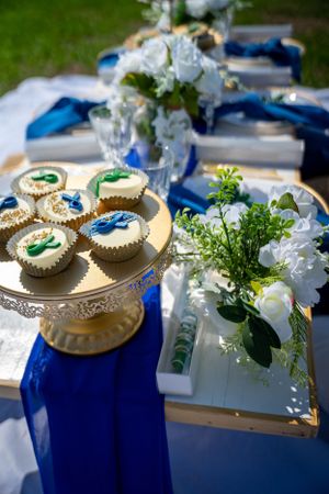 Elegant table setting with gold cupcake stand, white flowers, and royal blue table runners.