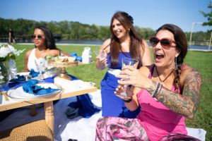 Guests socializing at a sunny outdoor event with decorated tables and floral centerpieces.