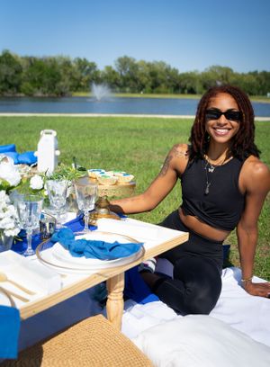 A picnic spread on a white tablecloth with drinks and snacks set against a sunny outdoor backdrop.