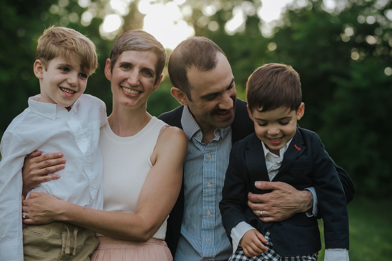 Family of four sharing tender moment outdoors during golden hour portrait session.
