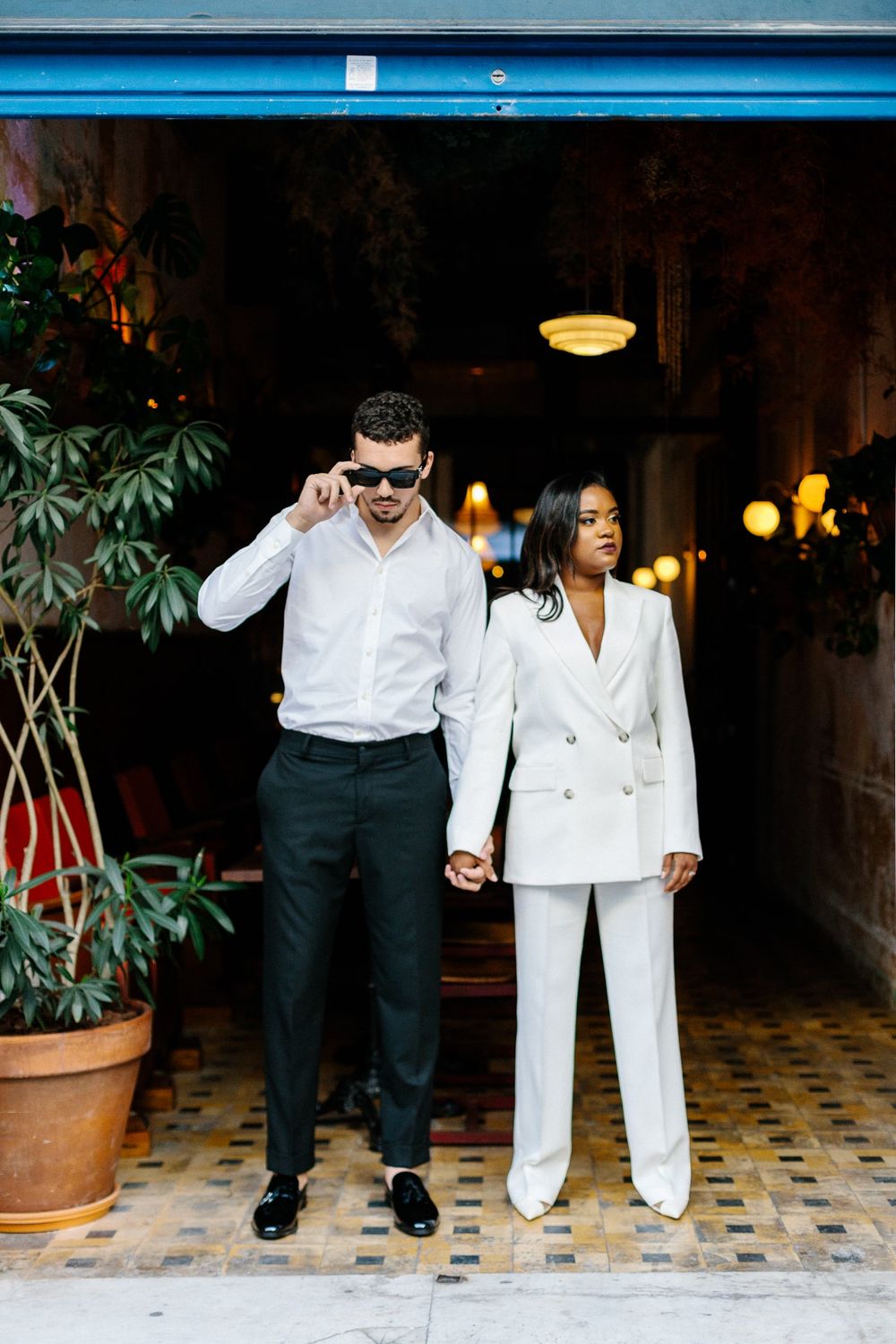 Couple in coordinated white outfits standing near potted plants.