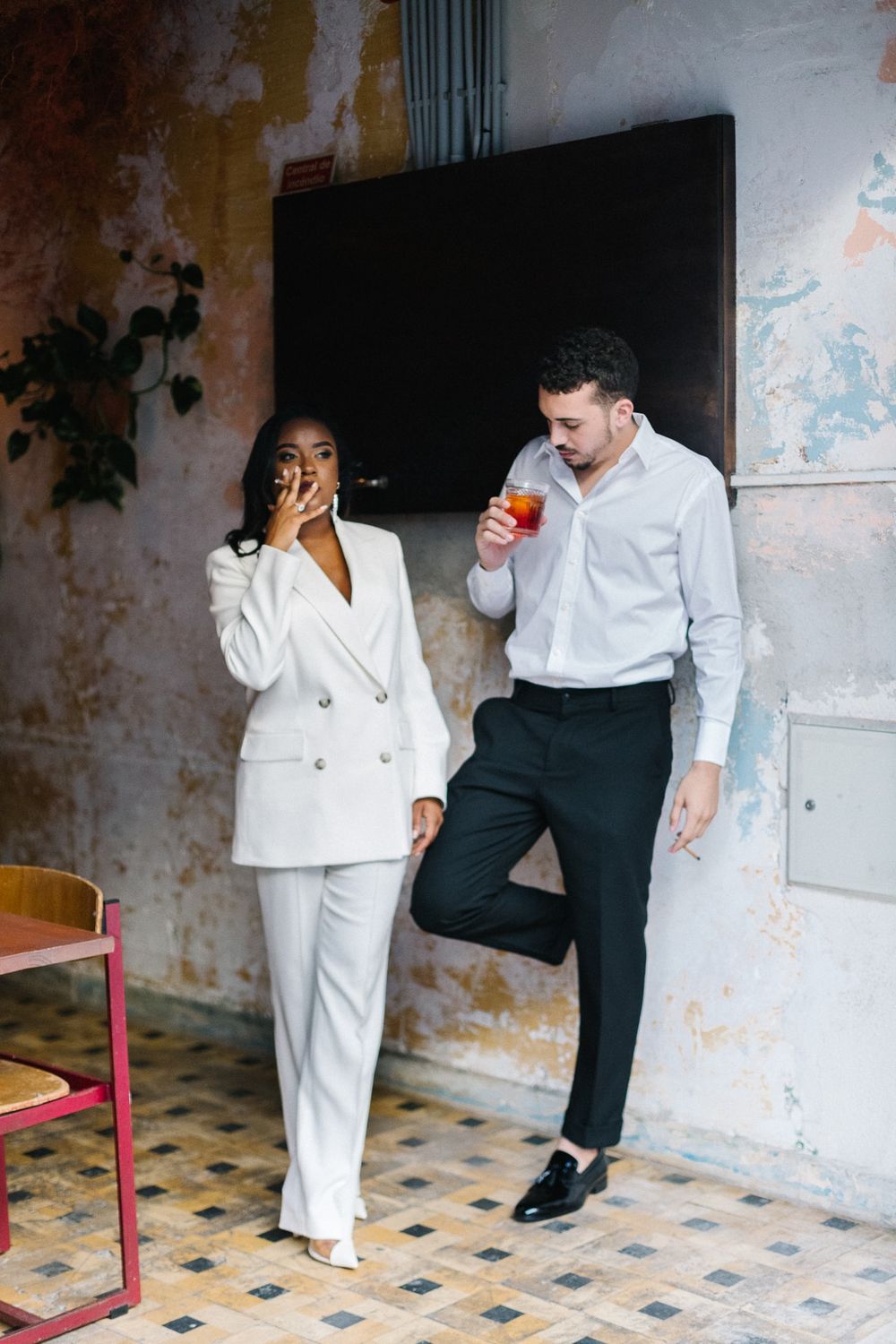 Stylish couple sharing drinks against weathered wall background.