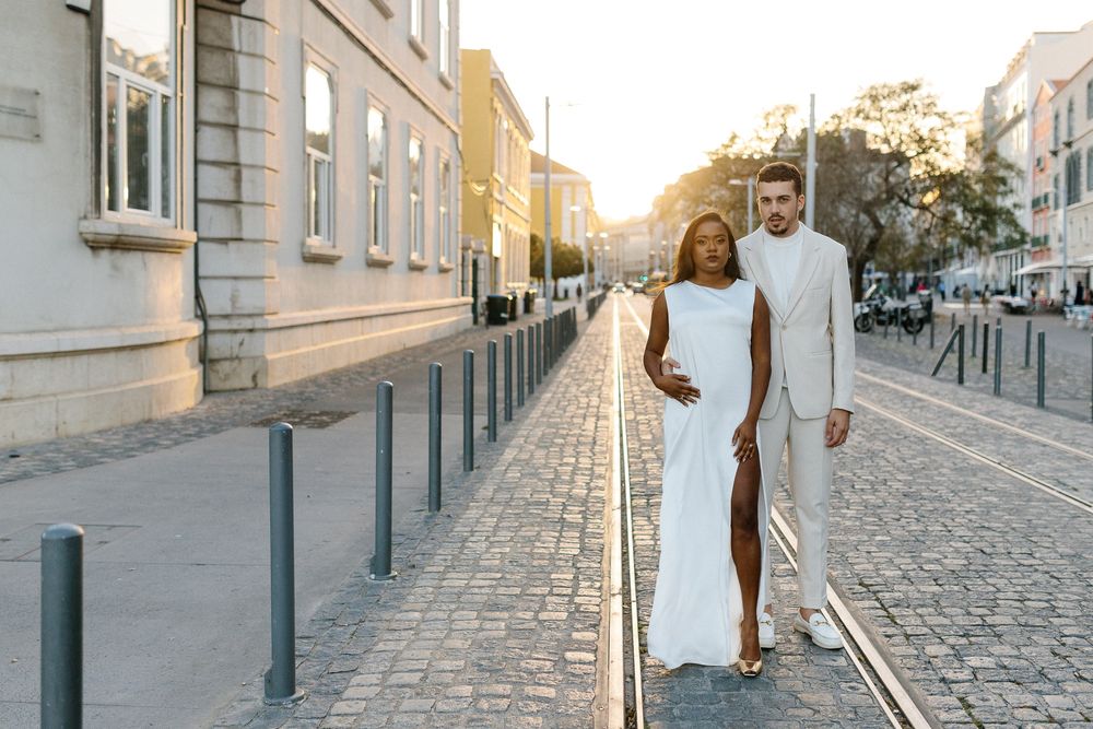 Couple in white outfits walking together on cobblestone street at sunset.