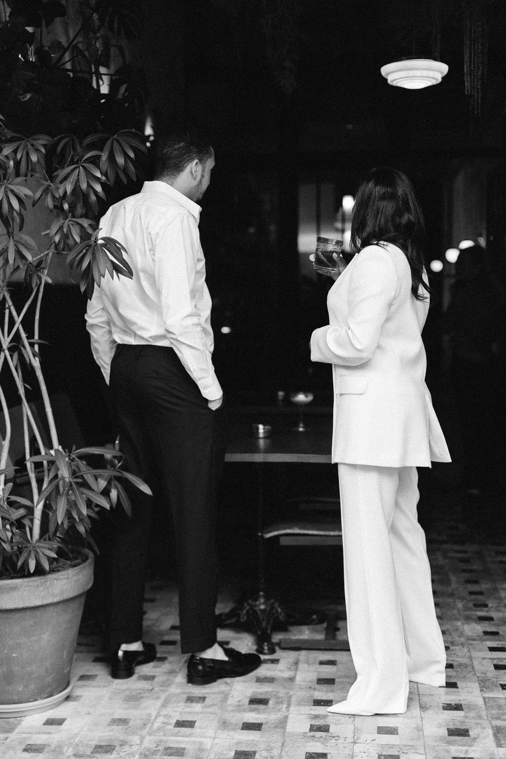 Couple in white outfits standing in dimly lit restaurant interior.