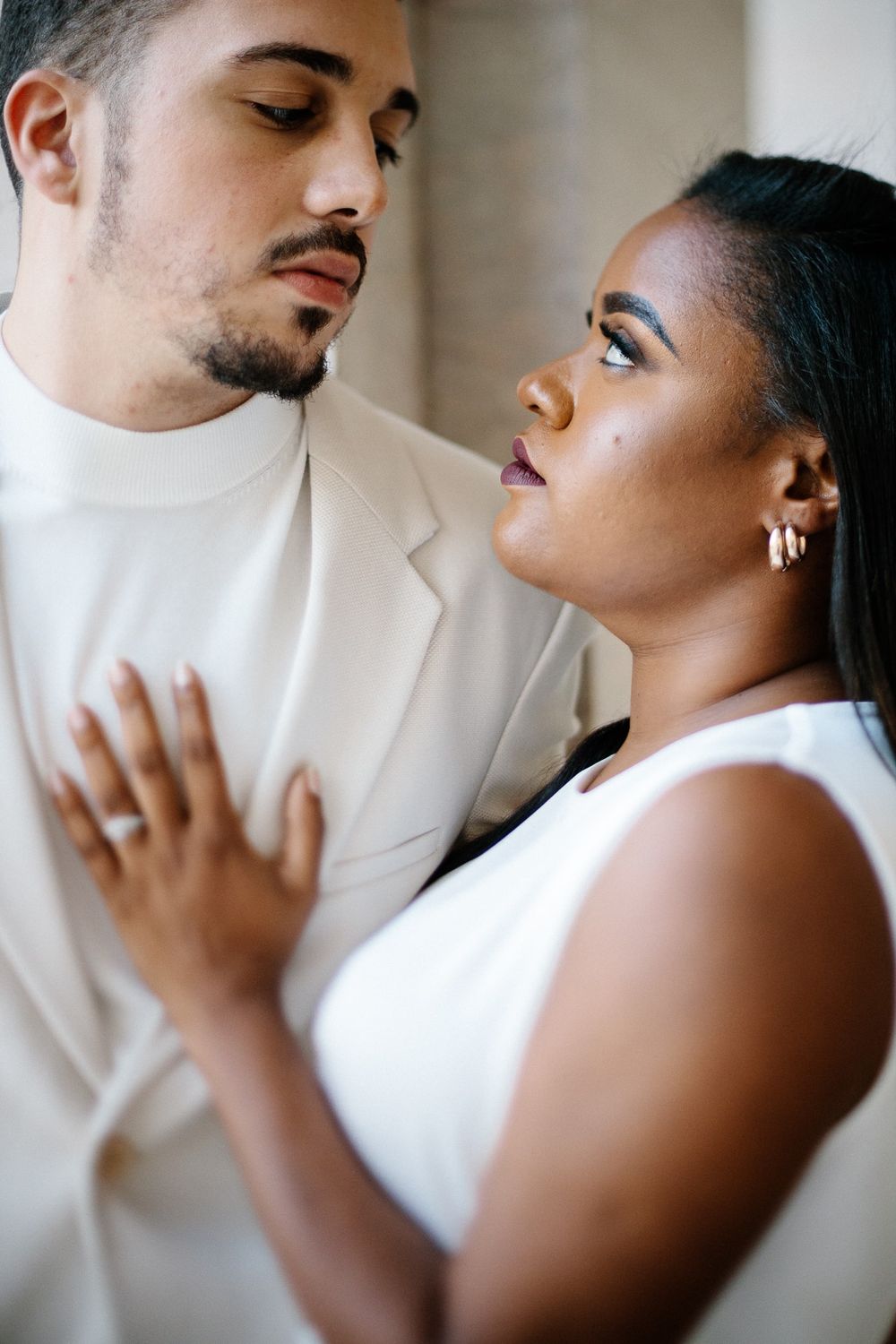 Close-up portrait of couple in white sharing an intimate moment against a light background.