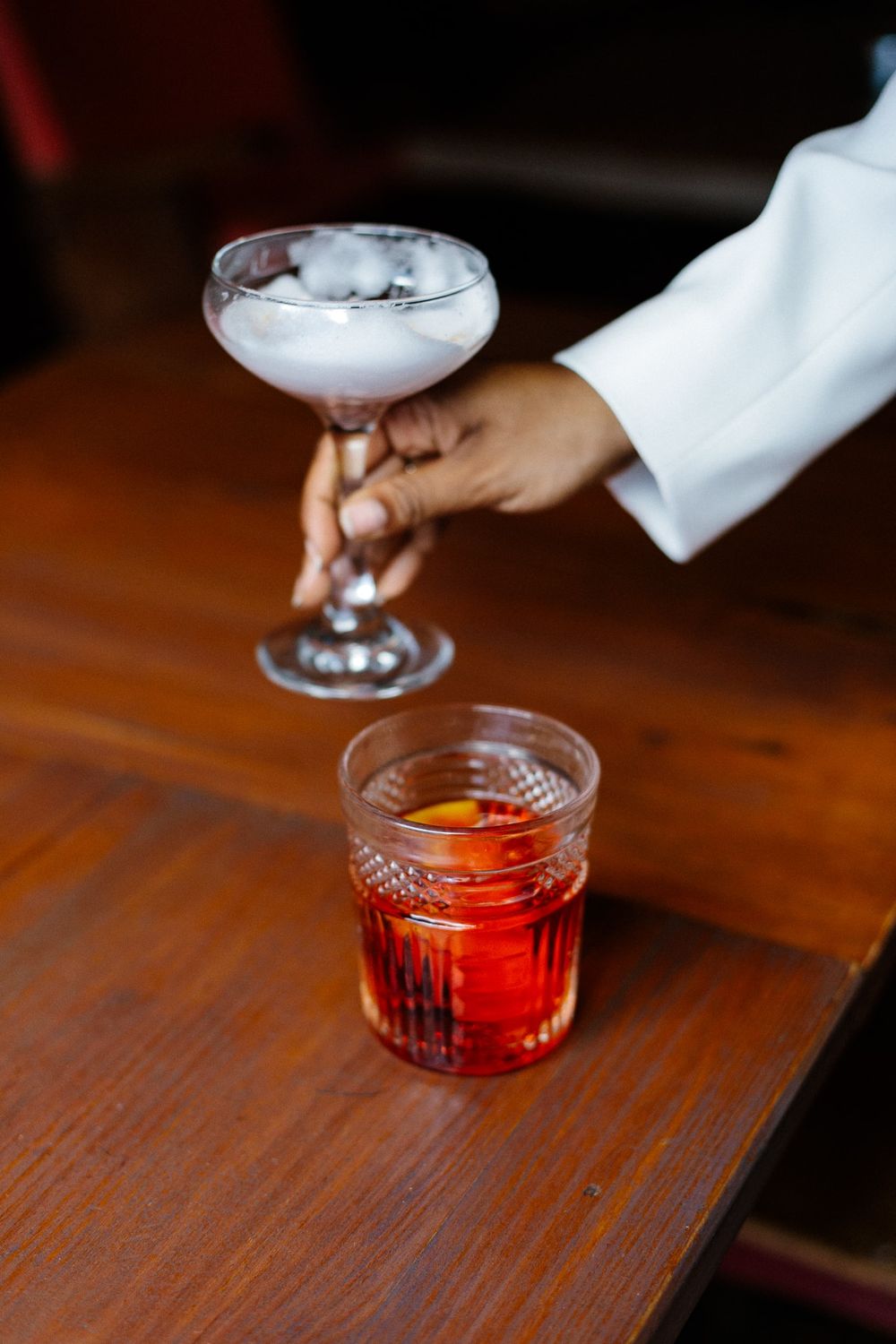 Two elegant cocktails on wooden bar top with one frosted glass and one red drink.