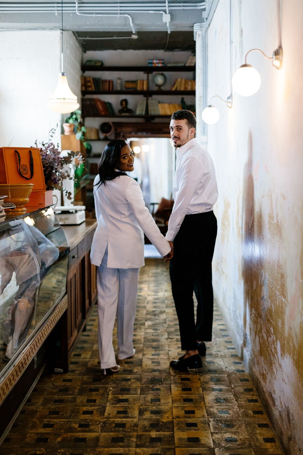 Stylish couple holding hands while walking through vintage shop interior with tiled floor.