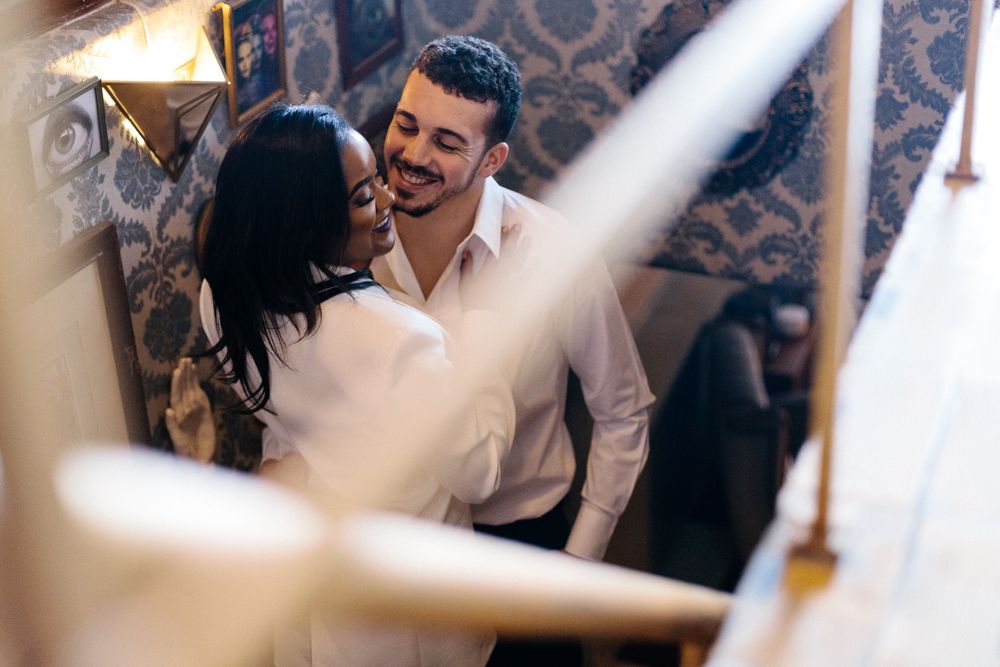 Couple laughing together in a warmly lit room with decorative wallpaper.