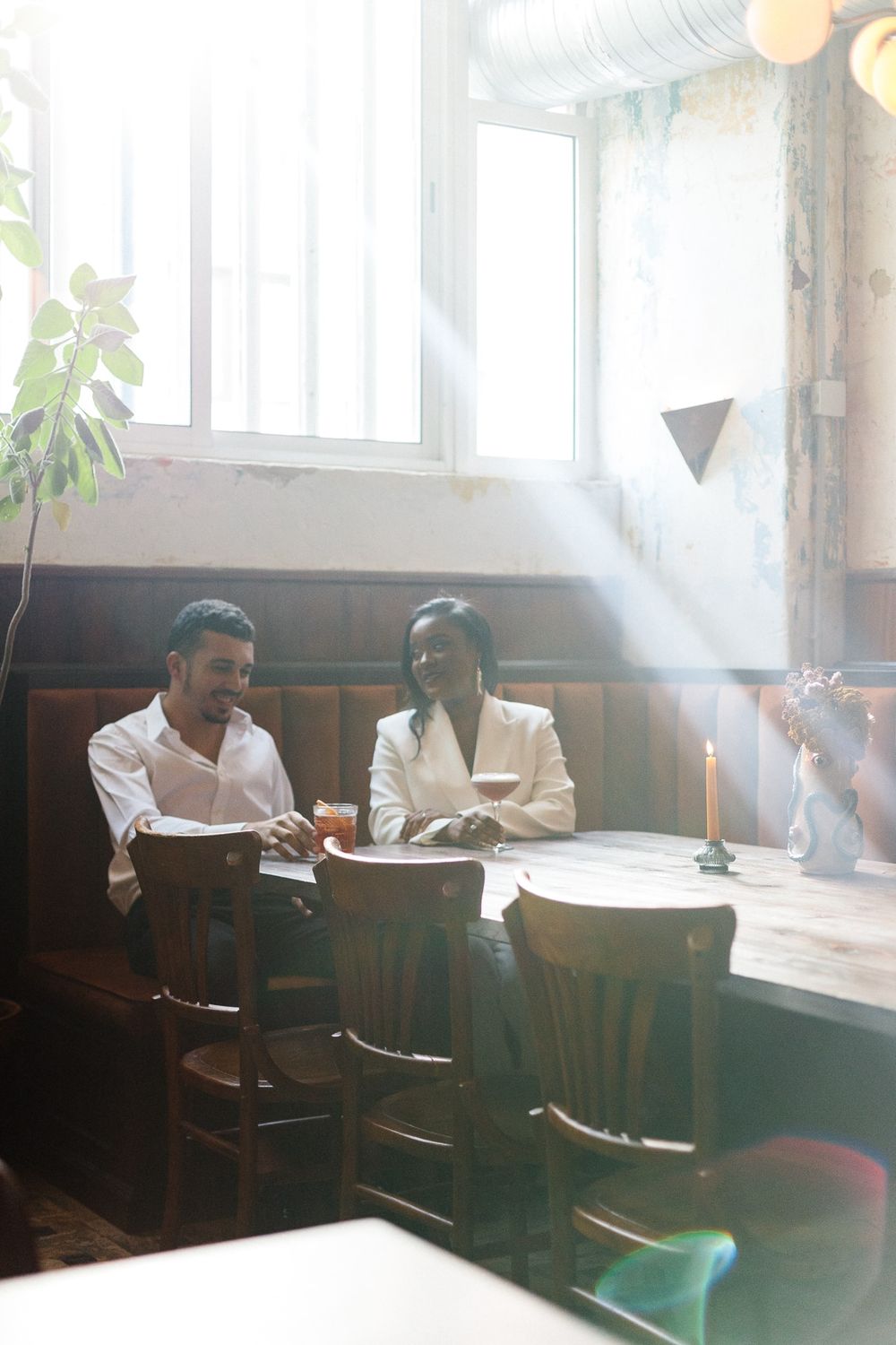 Couple seated at a sunlit restaurant booth enjoying drinks together.