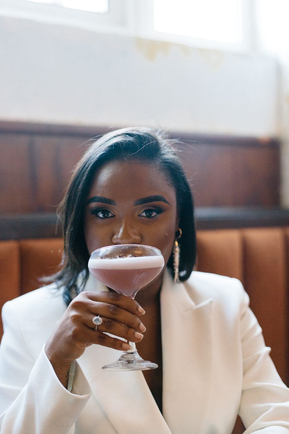 Elegant person in white blazer sipping a cocktail at a bar.