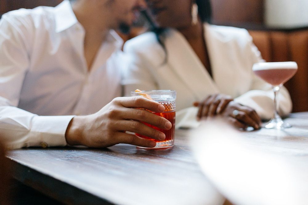 Hands holding cocktail glasses at a restaurant table.