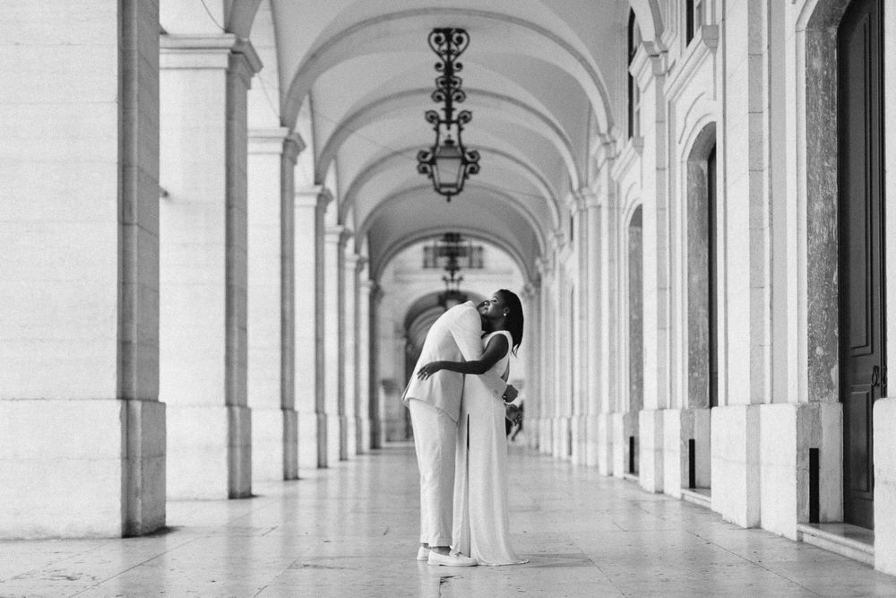Romantic couple embraces in an elegant arched colonnade with hanging lamps.