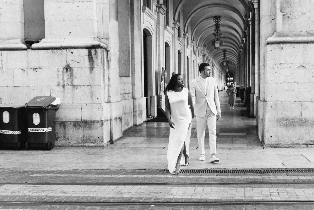 Black and white photograph of couple walking through an arched colonnade.