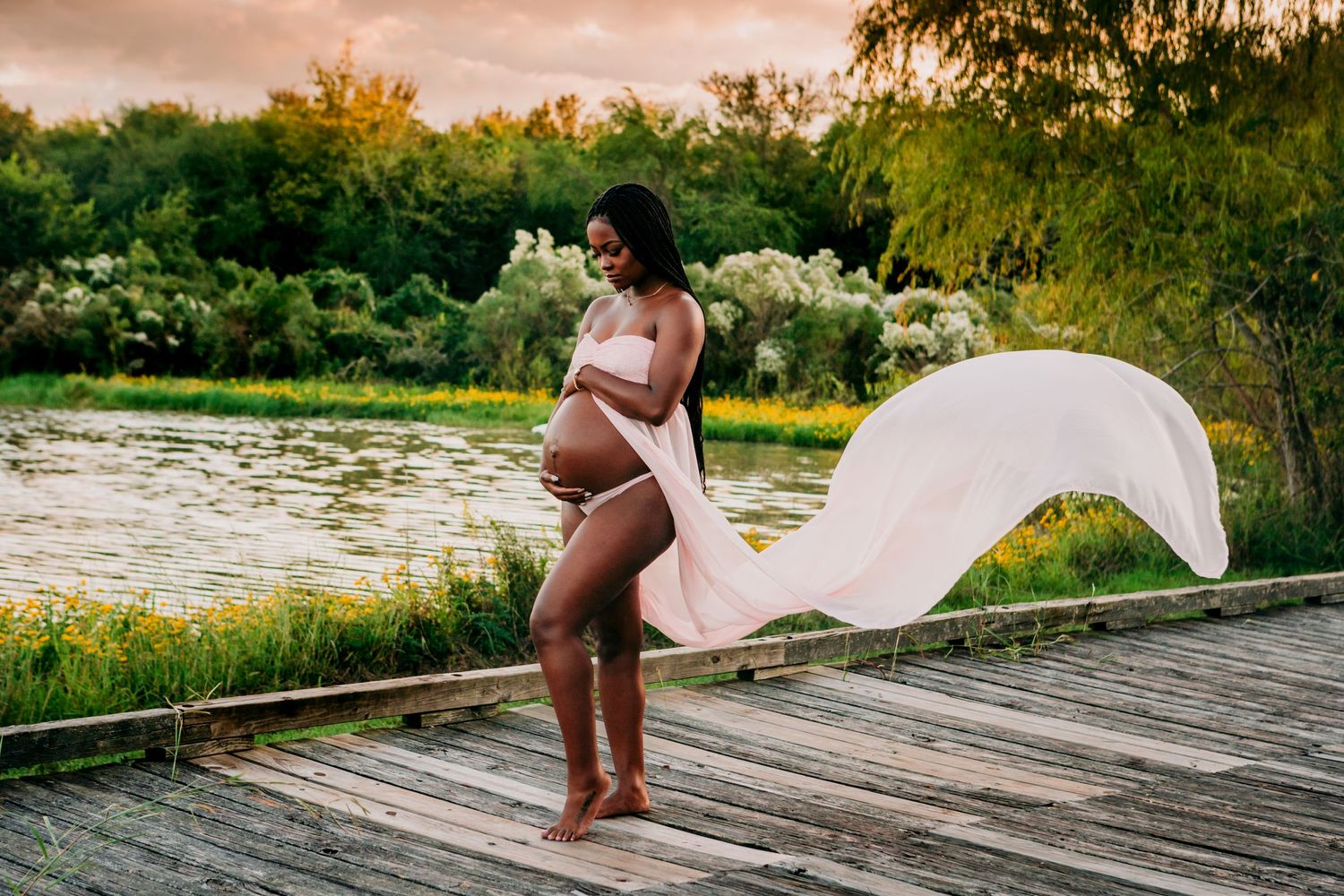 Flowing white fabric drapes gracefully on a wooden dock by a pond during golden sunset hour.