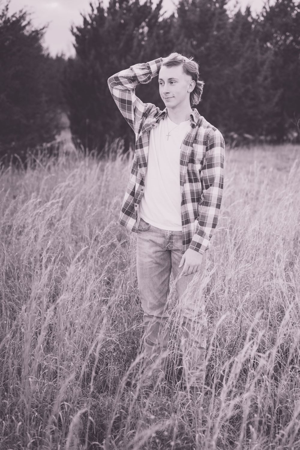 Black and white portrait of a young person standing in a field wearing a plaid shirt.