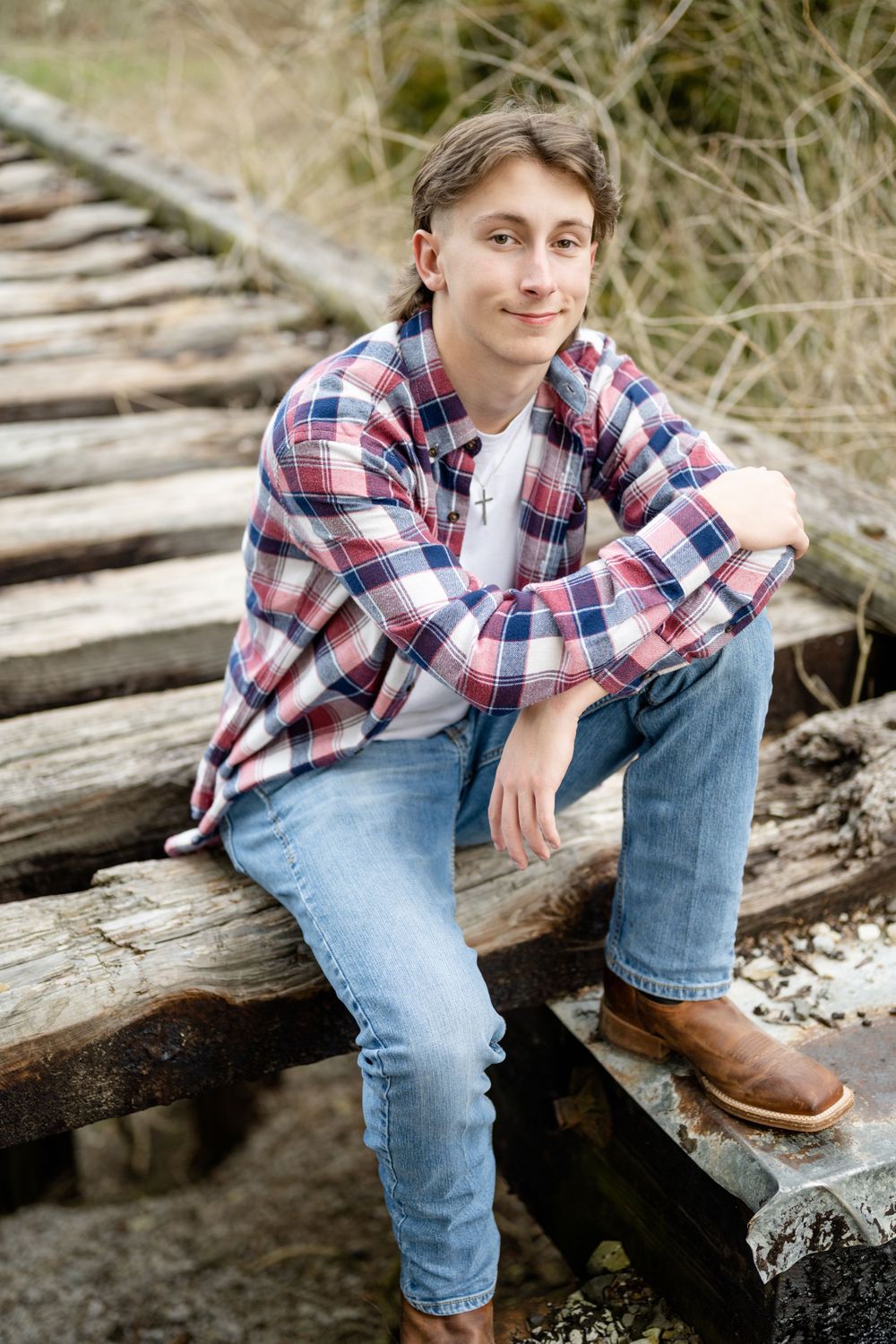 Portrait of a person in plaid shirt and jeans sitting on wooden railroad tracks.