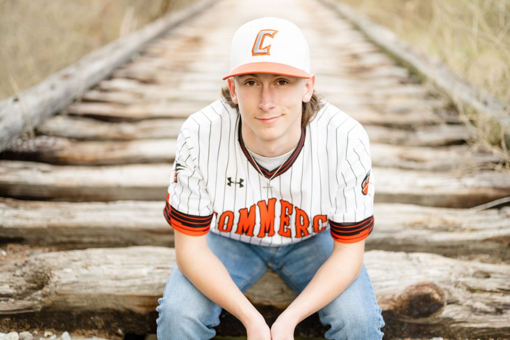 A baseball player sitting on railroad tracks wearing a white and orange uniform.