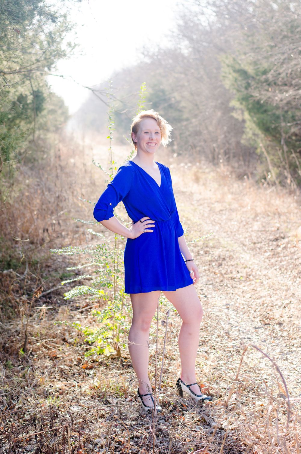 Person in vibrant blue dress poses on rustic nature path during golden hour.