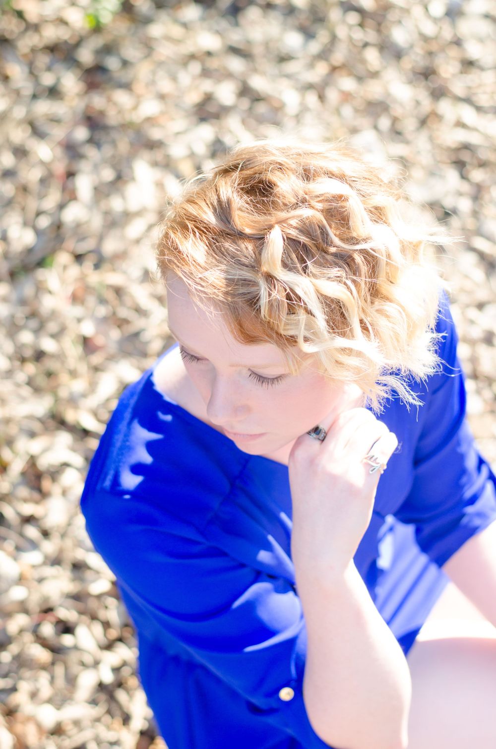 Artistic overhead portrait with bright blue shirt against autumn leaves.