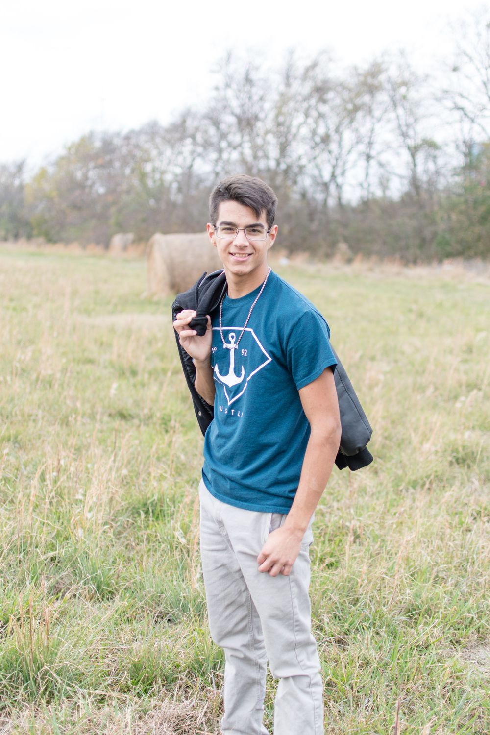 Person in teal anchor shirt posing with bag in field.