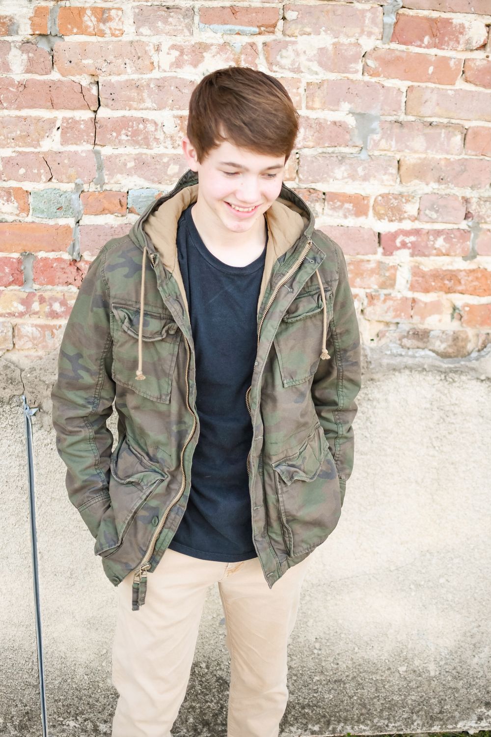 Casual portrait against brick wall wearing camo jacket and khaki pants.