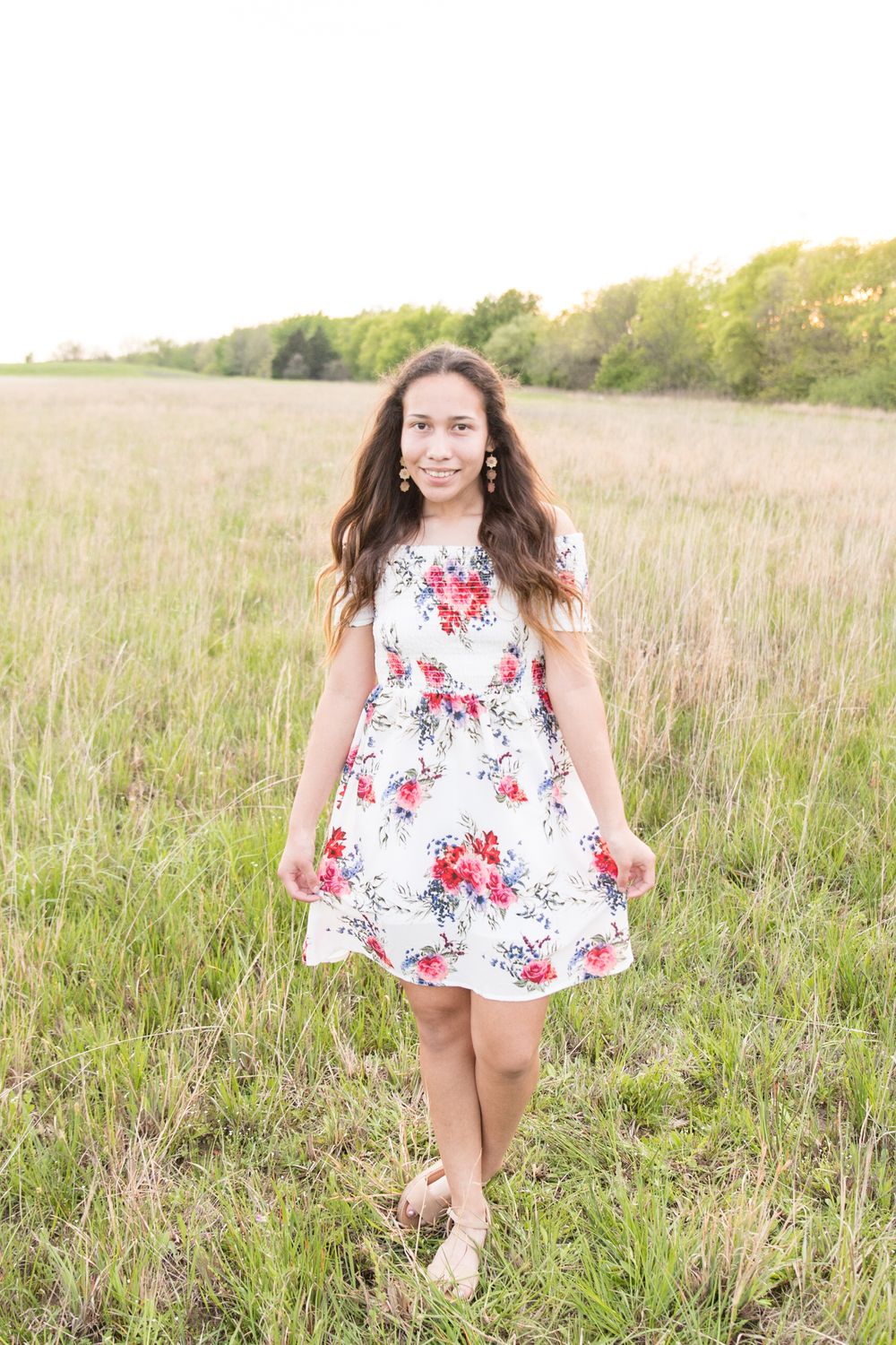 A figure in a white floral dress walks through a sun-drenched meadow at golden hour.