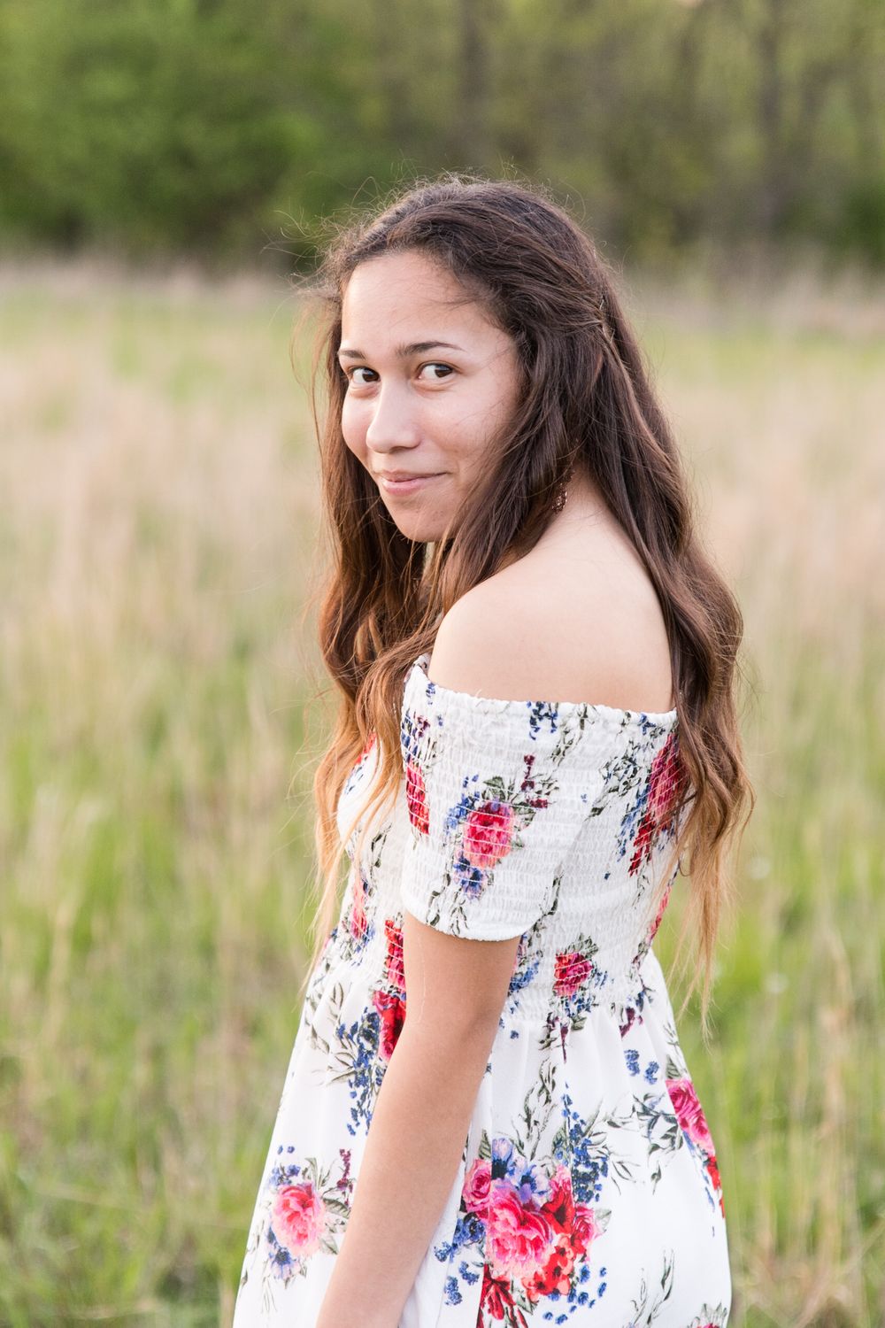 A person in a floral off-shoulder dress poses against a natural backdrop of tall grass.