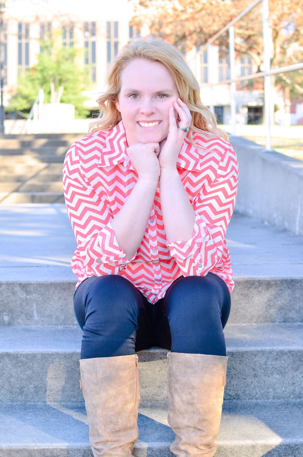 Person in pink chevron top and boots sitting on concrete steps outdoors.