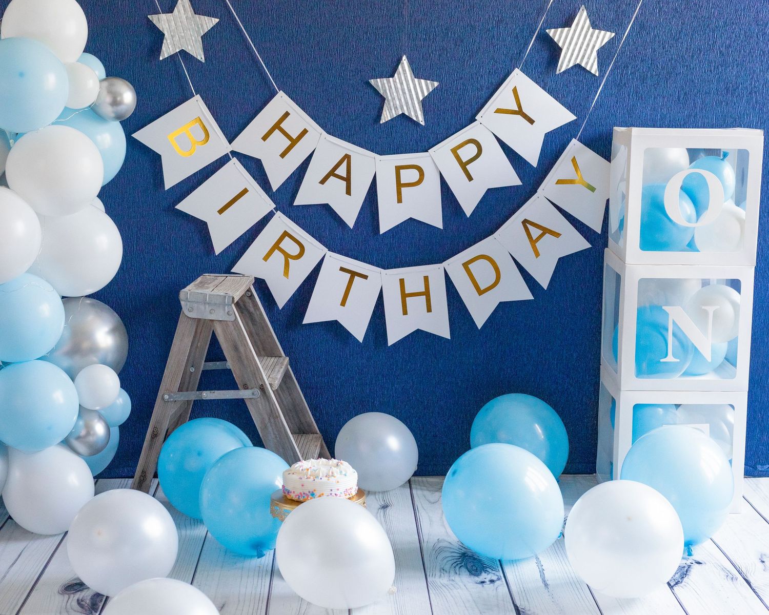 Birthday party backdrop with blue and white balloons, silver stars, and Happy Birthday banner.