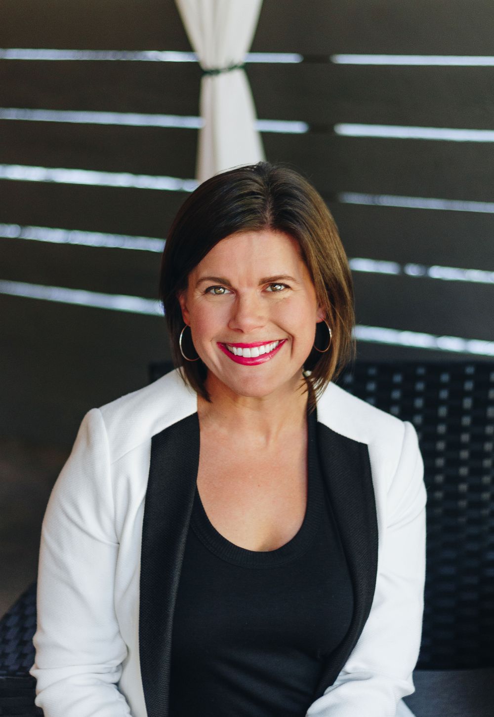 Professional portrait in white blazer and black top against dark background.