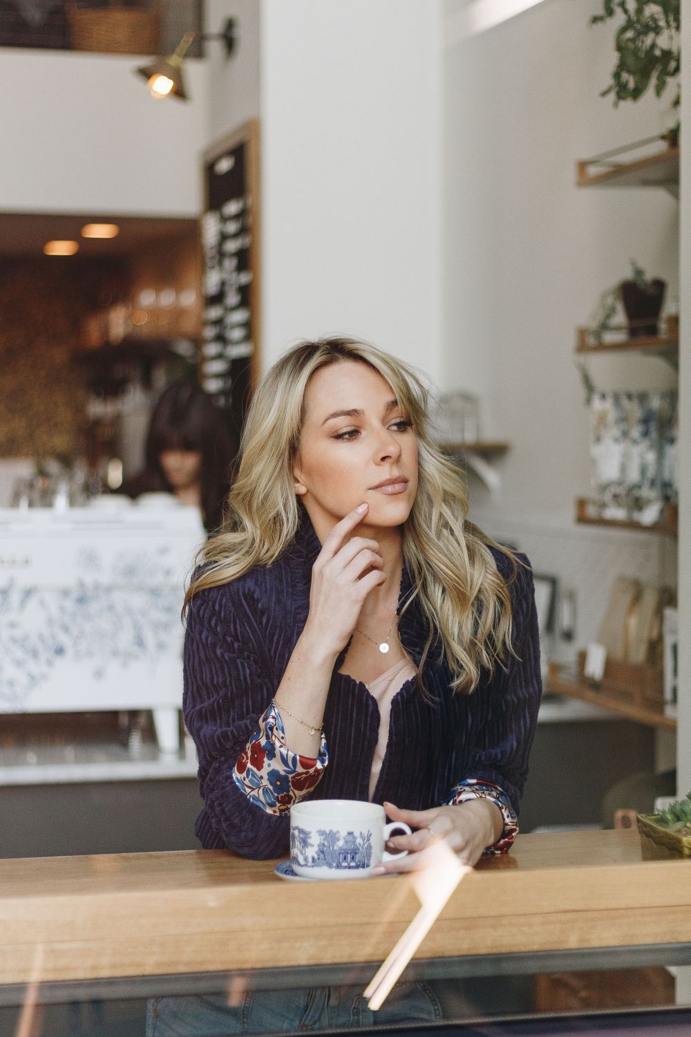 Sitting thoughtfully at a cafe counter with a coffee cup in a navy blazer.