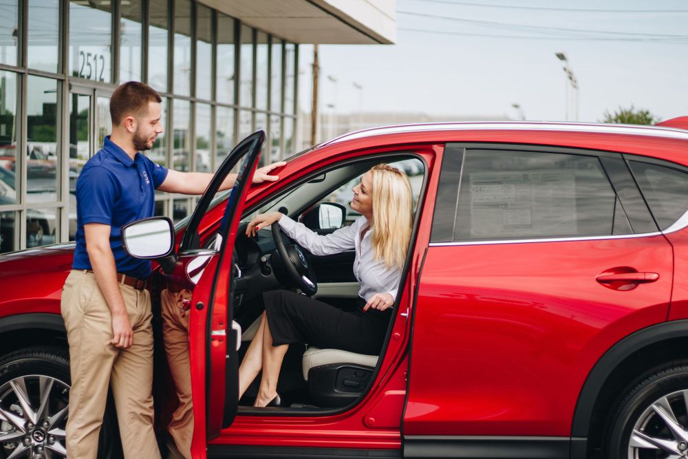 Car salesperson assisting customer at dealership with red SUV.