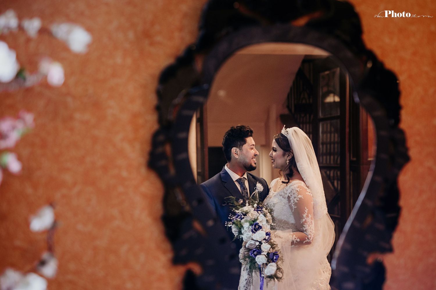 Artistic wedding portrait through ornate frame with orange wall background.