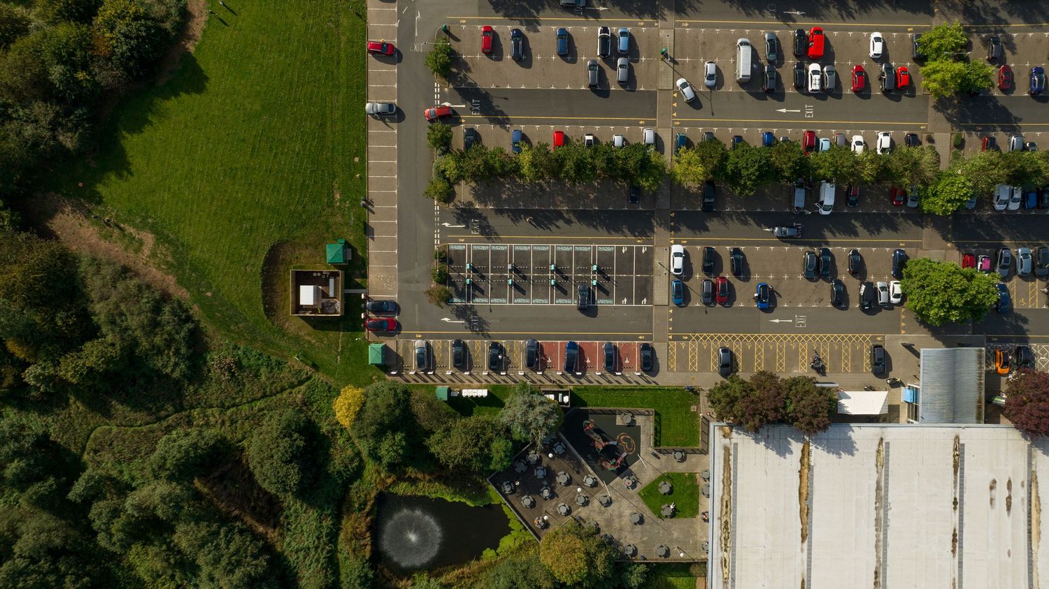 Bird's eye view of a parking lot with cars adjacent to green space and buildings.